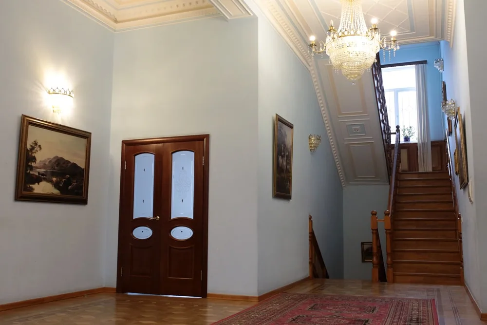 Светлый холл с деревянной лестницей, картины на стенах
